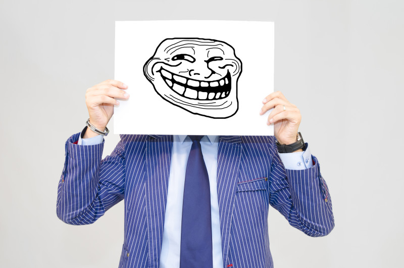 Business man hoding card with troll face isolated on grey background