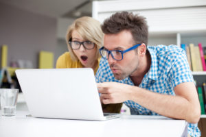 Two surprised students learning in library on laptop