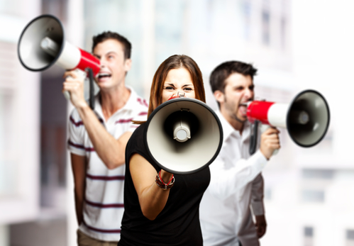 portrait of a angry group of employees shouting using megaphones against a city background